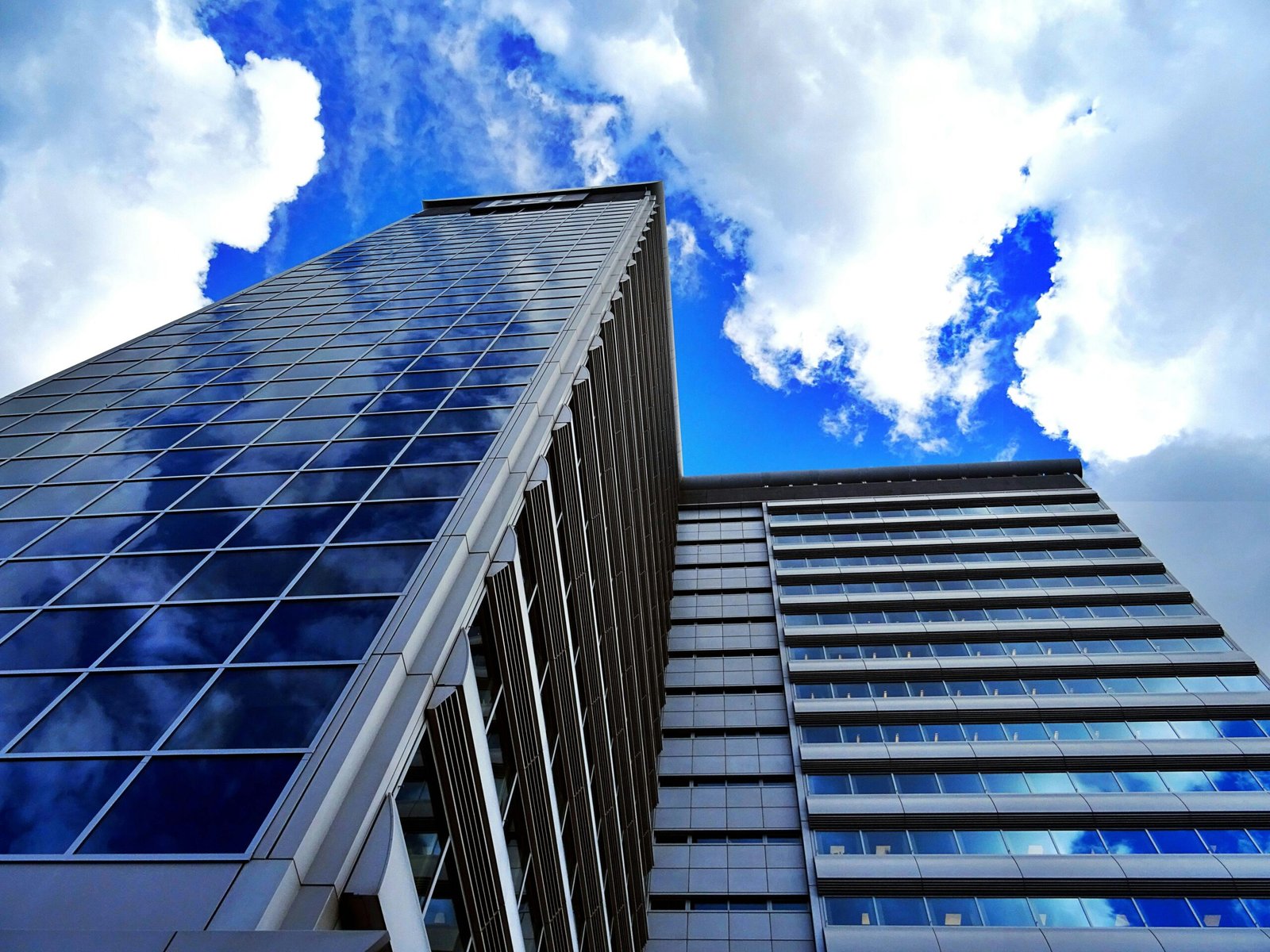 Low angle view of a modern skyscraper reflecting blue sky and clouds, showcasing urban architecture.